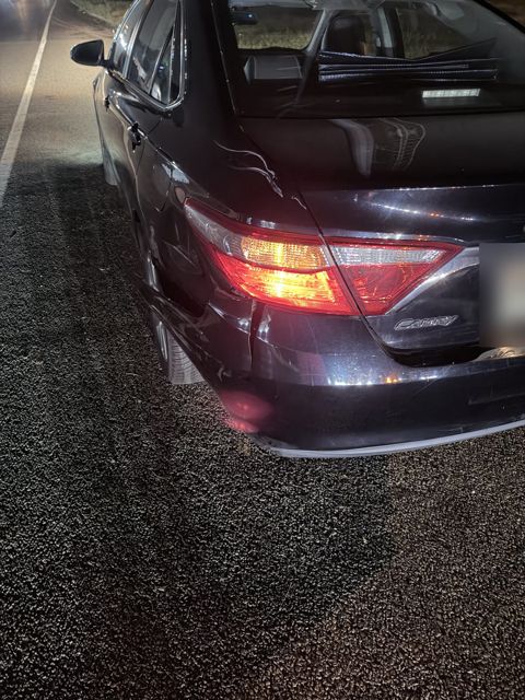 V1 at the scene at night, stopped on the right shoulder, showing left rear damage